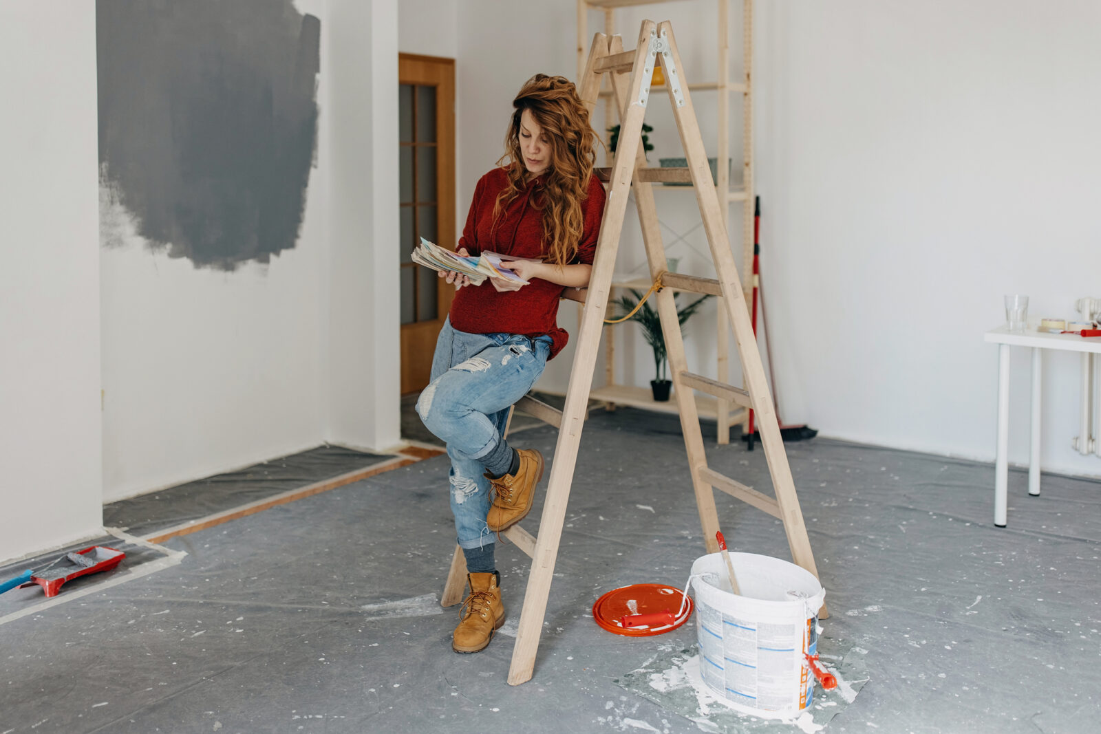 Vrouw leunt tegen ladder tijdens het kiezen van verfkleur voor onderhoud aan woning