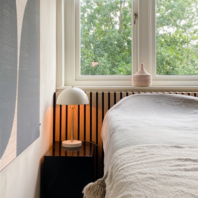 Moderne tafellamp met ronde kap op nachtkastje naast bed in lichte slaapkamer