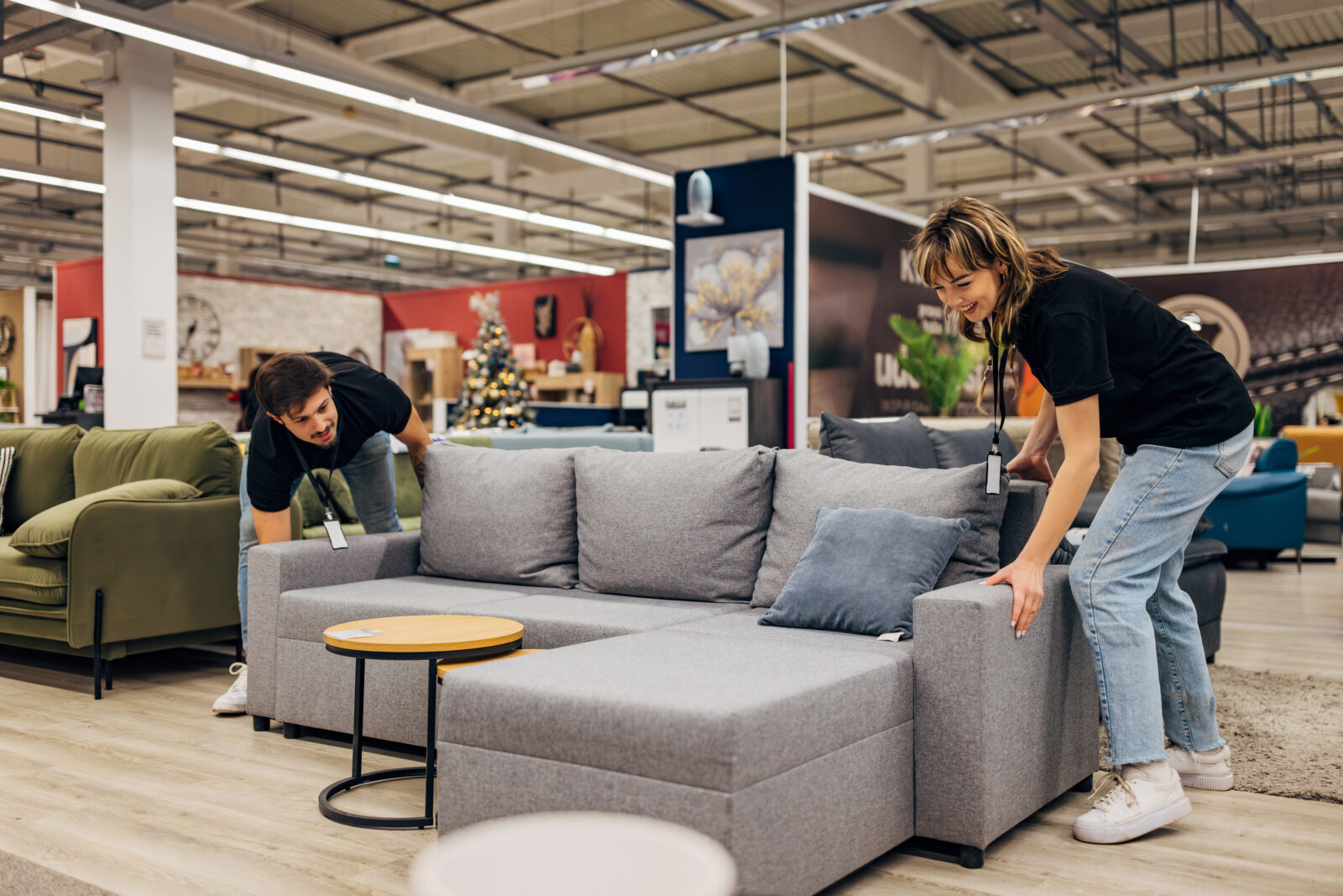 Twee mensen testen een grijze zitbank in een meubelshowroom om het zitcomfort te beoordelen.