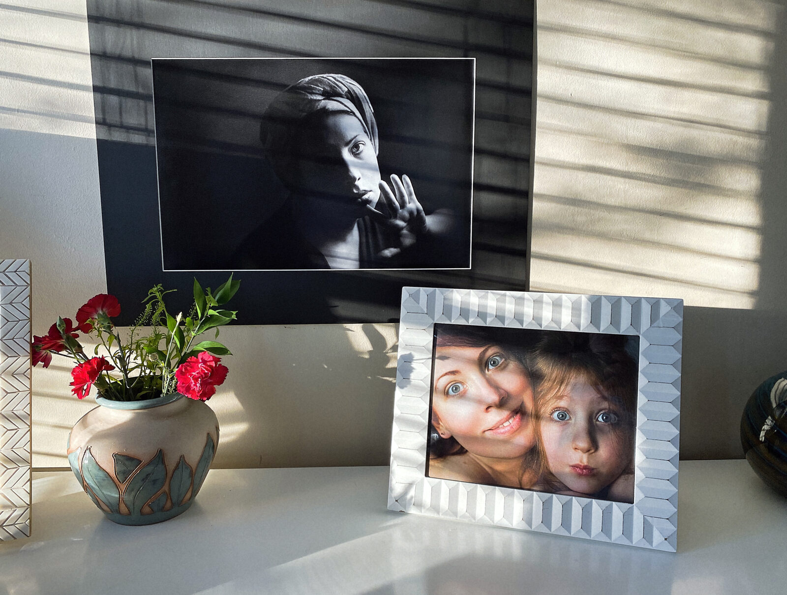 Fotolijstjes met familiefoto’s in zacht zonlicht op een dressoir, een warme en persoonlijke sfeer in huis.