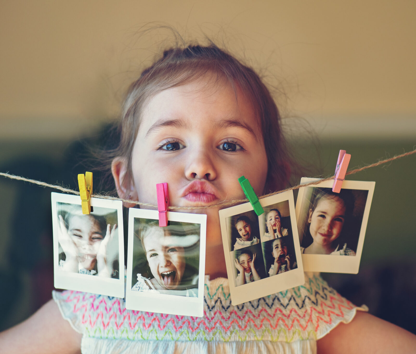 Klein meisje met familiefoto’s aan een lijn, lachend en speels voor de camera.