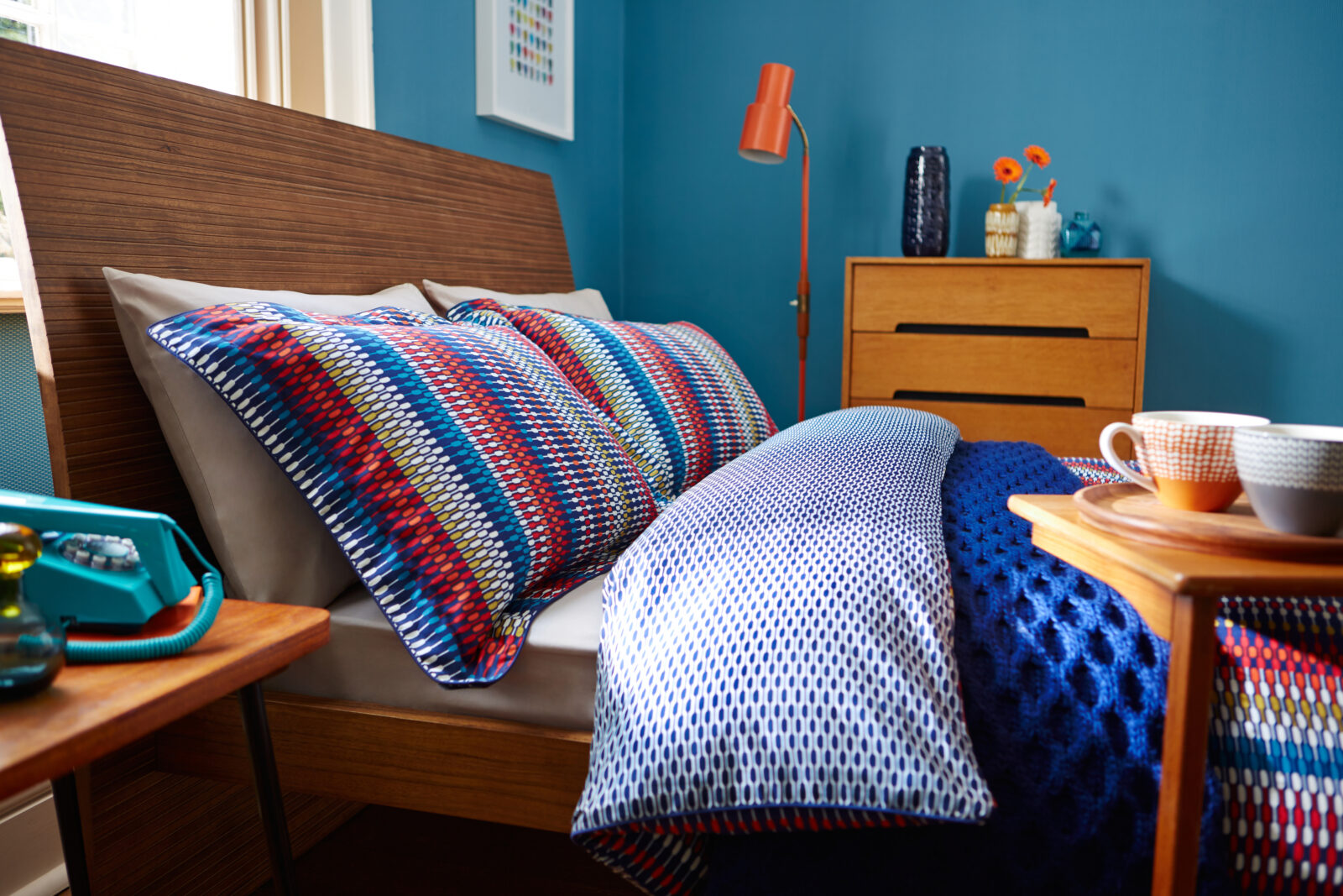 Slaapkamer met blauw beddengoed, houten meubels en kleurrijke accenten