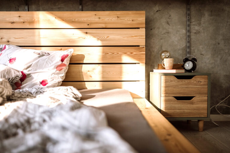 Licht en rustige slaapkamer met houten bed, nachtkastje en warm zonlicht door het raam