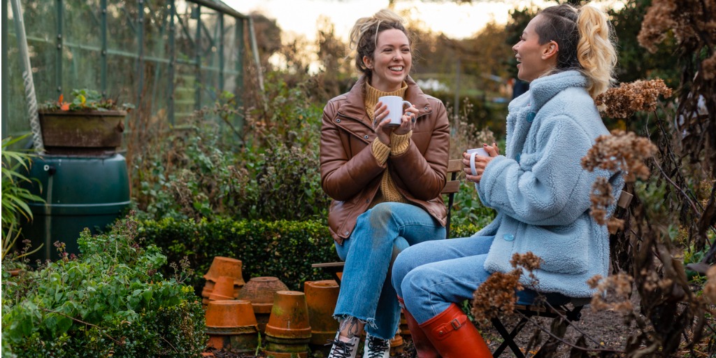 Twee vrouwen drinken koffie in een tuin met regenton op de achtergrond