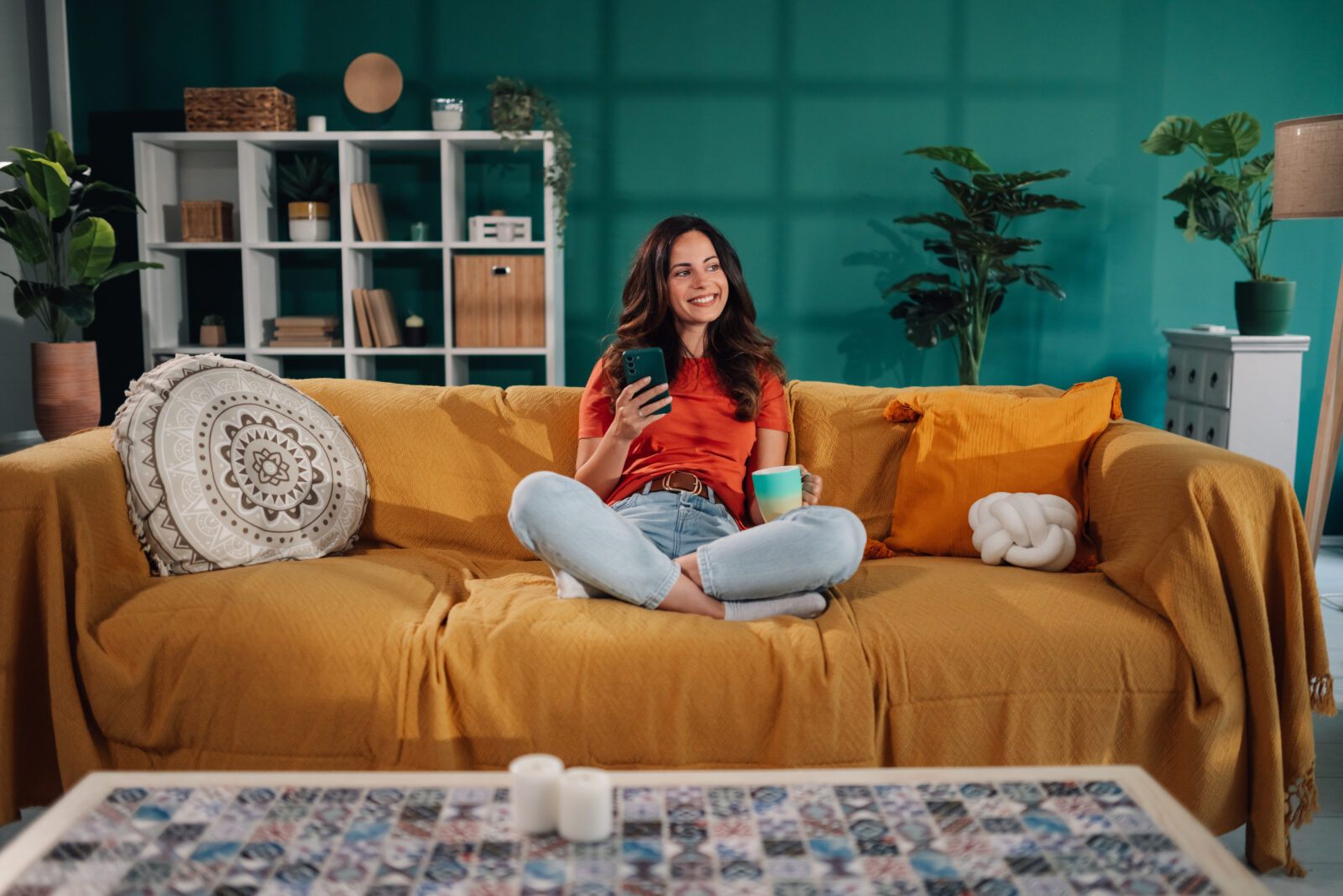 Vrouw op gele bank in woonkamer met groene muur en planten.