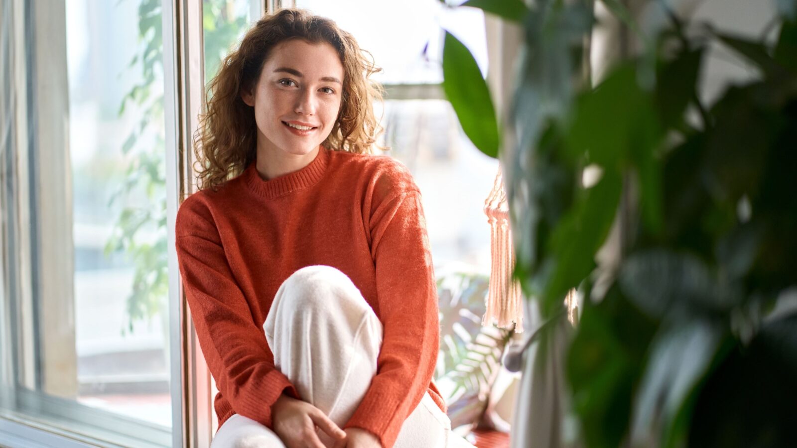 Vrouw zit ontspannen bij een goed geïsoleerd raam in een warme woonkamer terwijl buiten het koud is.