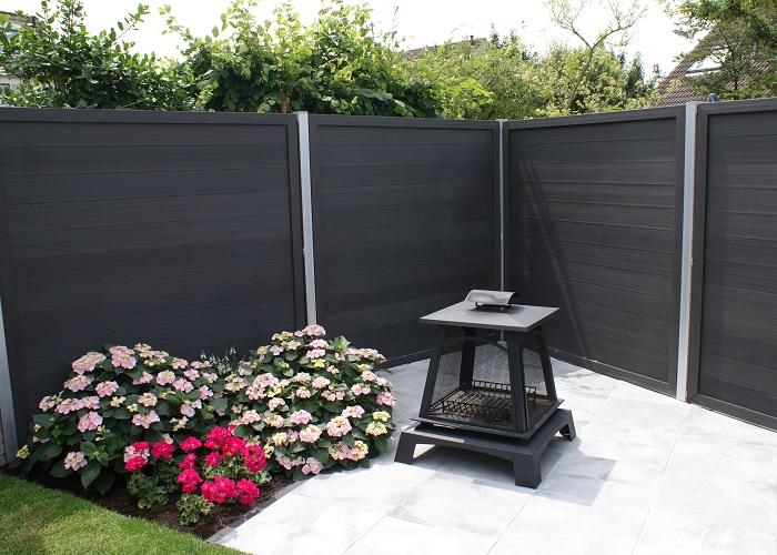Moderne tuin met donkere composiet schutting, bloemenborder en een compacte vuurkorf
