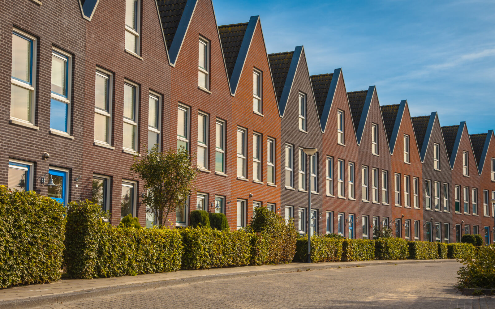 Moderne rij nieuwbouwwoningen met puntdaken in een rustige woonwijk.
