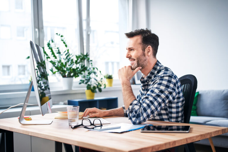 Man aan een houten bureau met laptop in een lichte ruimte met planten en daglicht