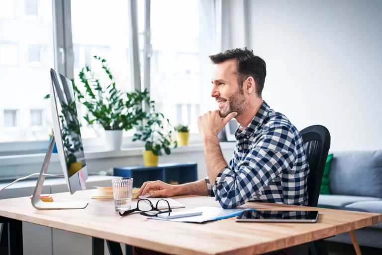 Man aan een houten bureau met laptop in een lichte ruimte met planten en daglicht
