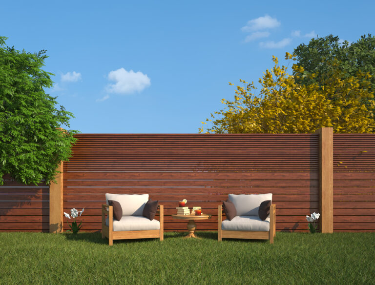 Moderne tuin met een houten schutting en twee comfortabele stoelen in het zonlicht