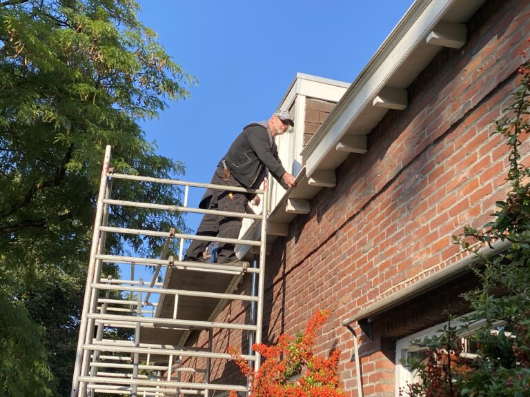 Vakman op steiger bezig met onderhoud aan een oud bakstenen huis.