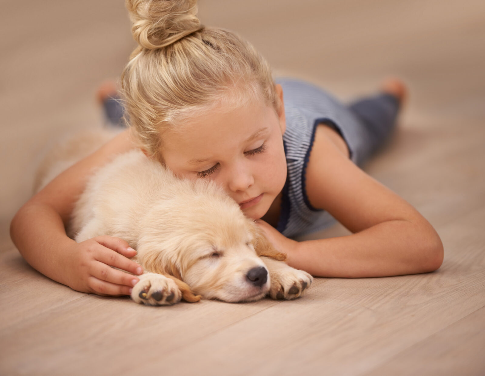 Klein meisje dat met gesloten ogen tegen een slapende puppy op een lichte houten vloer ligt.