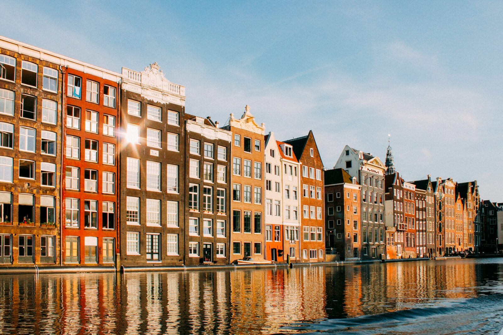 Rij grachtenpanden aan het water in Amsterdam bij ochtendlicht.