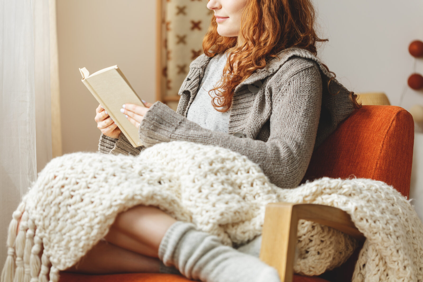 Vrouw die onder een warme deken zit te lezen in een knusse woonkamer voor extra comfort zonder de verwarming hoger te zetten.
