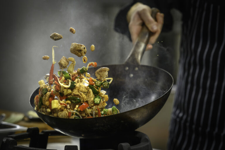 Chef bereidt roerbakgerecht in wok op hoge temperatuur in professionele keuken