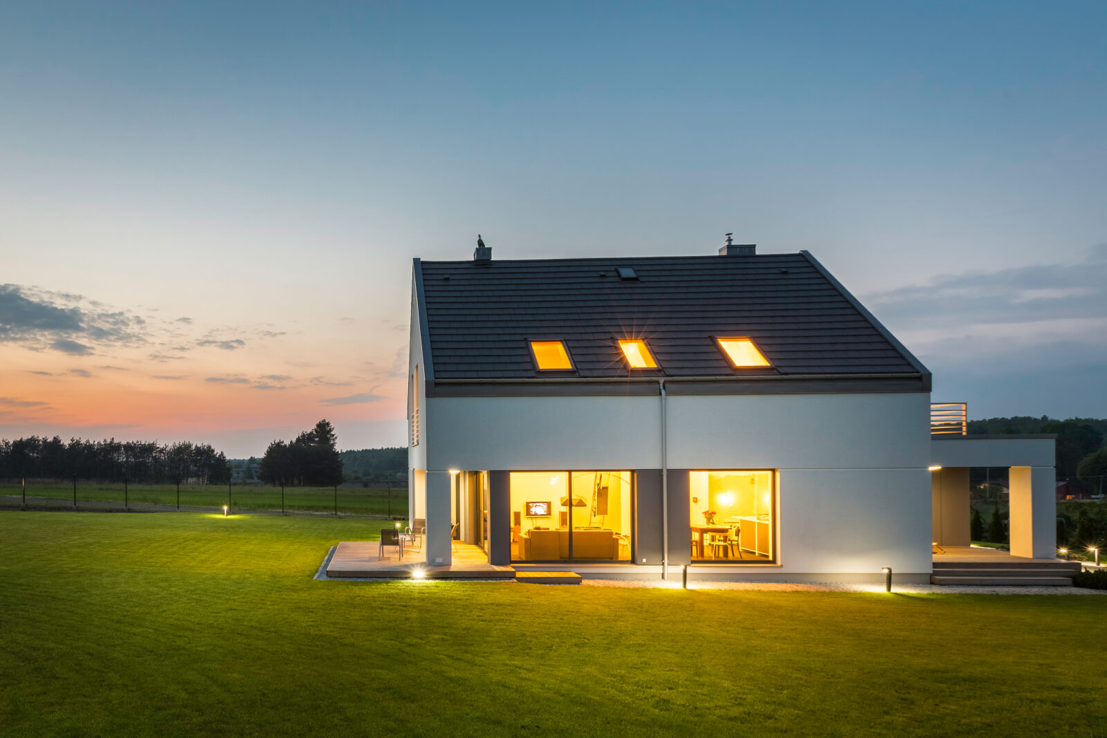 Moderne woning in de avond met buitenverlichting en verlichte ramen, passend bij praktische woningbeveiliging.