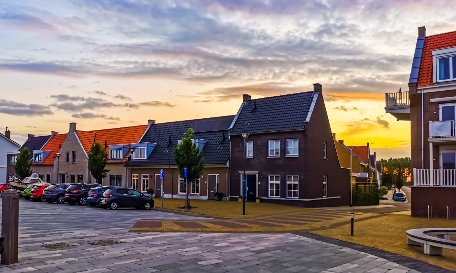 Nederlandse woonwijk met rijwoningen bij zonsondergang, gezien vanaf een rustige straat.