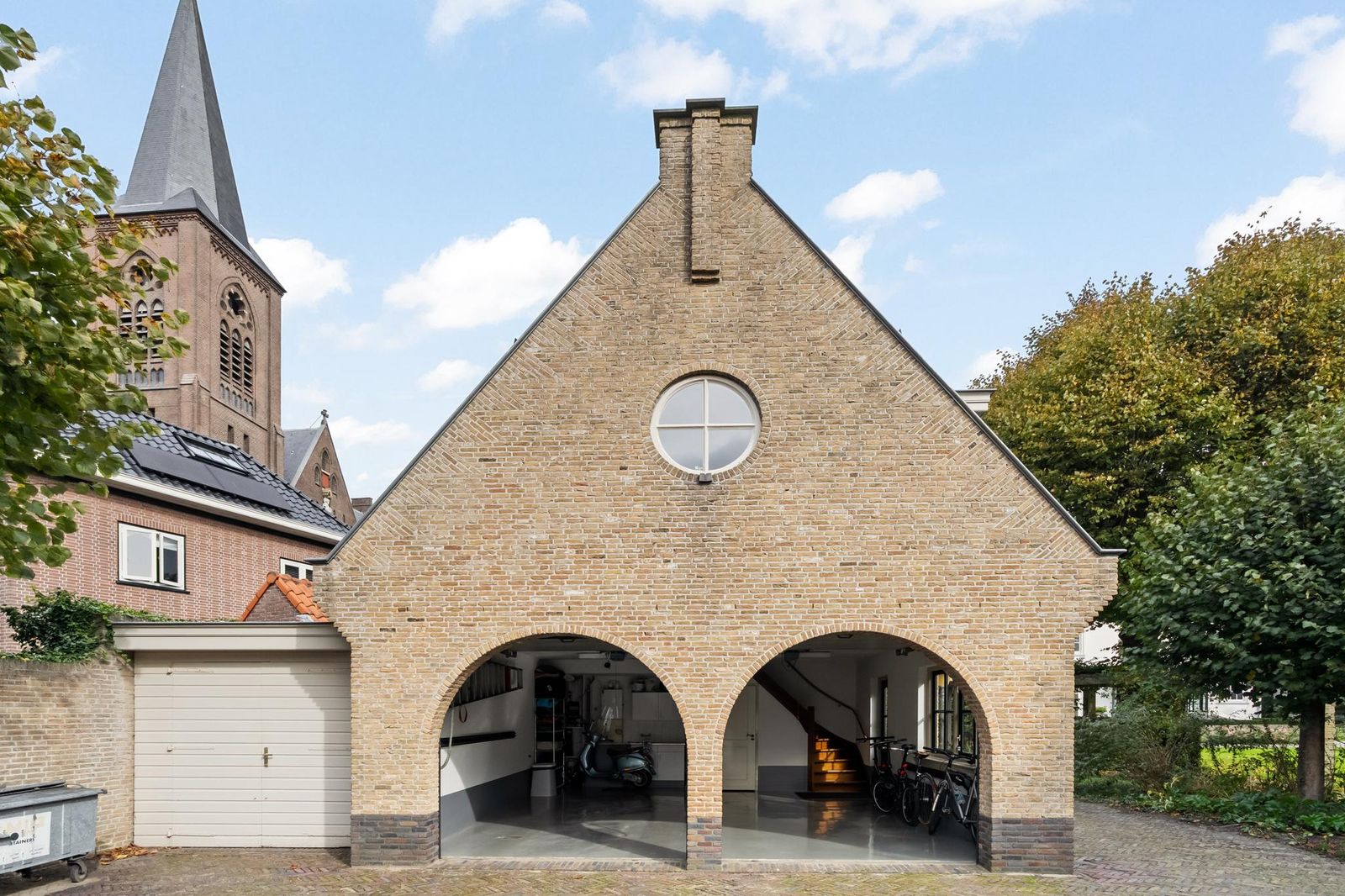 Vrijstaand garagegebouw van Lindenhof in Noordwijk met bakstenen gevel, ronde bogen en uitzicht op de kerk