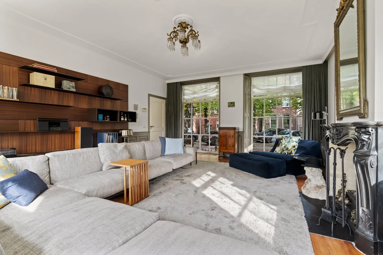 Woonkamer van rijksmonument Lindenhof in Noordwijk met klassieke schouw, hoge ramen en zicht op het Lindenplein