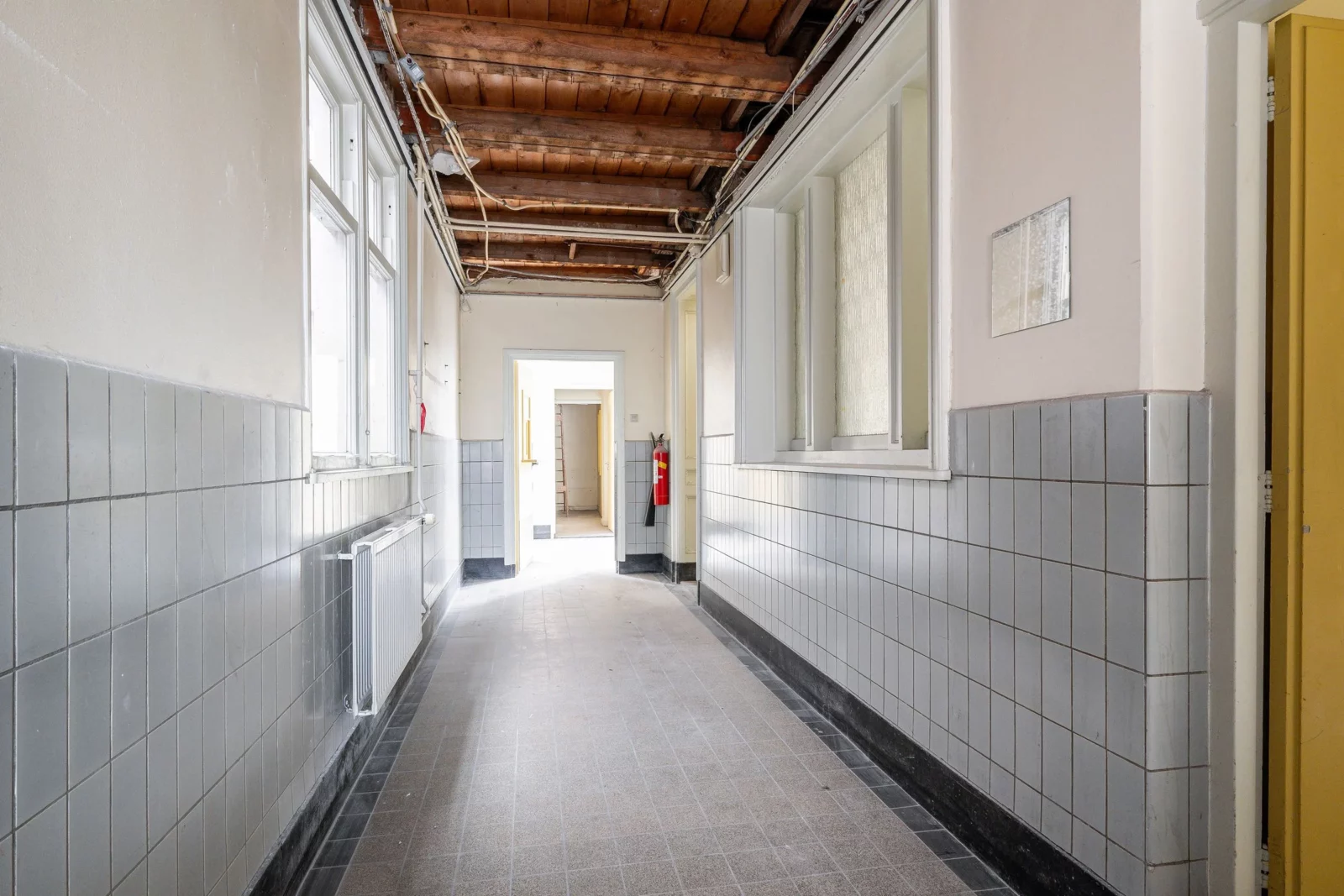Lange gang in voormalig politiebureau Hoflaan 134 met zichtlijnen, tegelwanden en open plafondconstructie