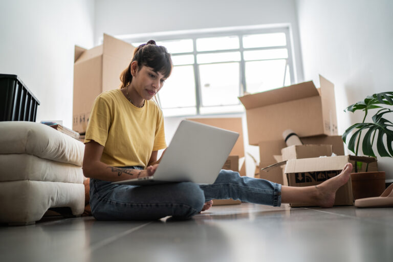 Persoon zit tussen verhuisdozen met laptop en denkt na over het kopen en financieren van een woning