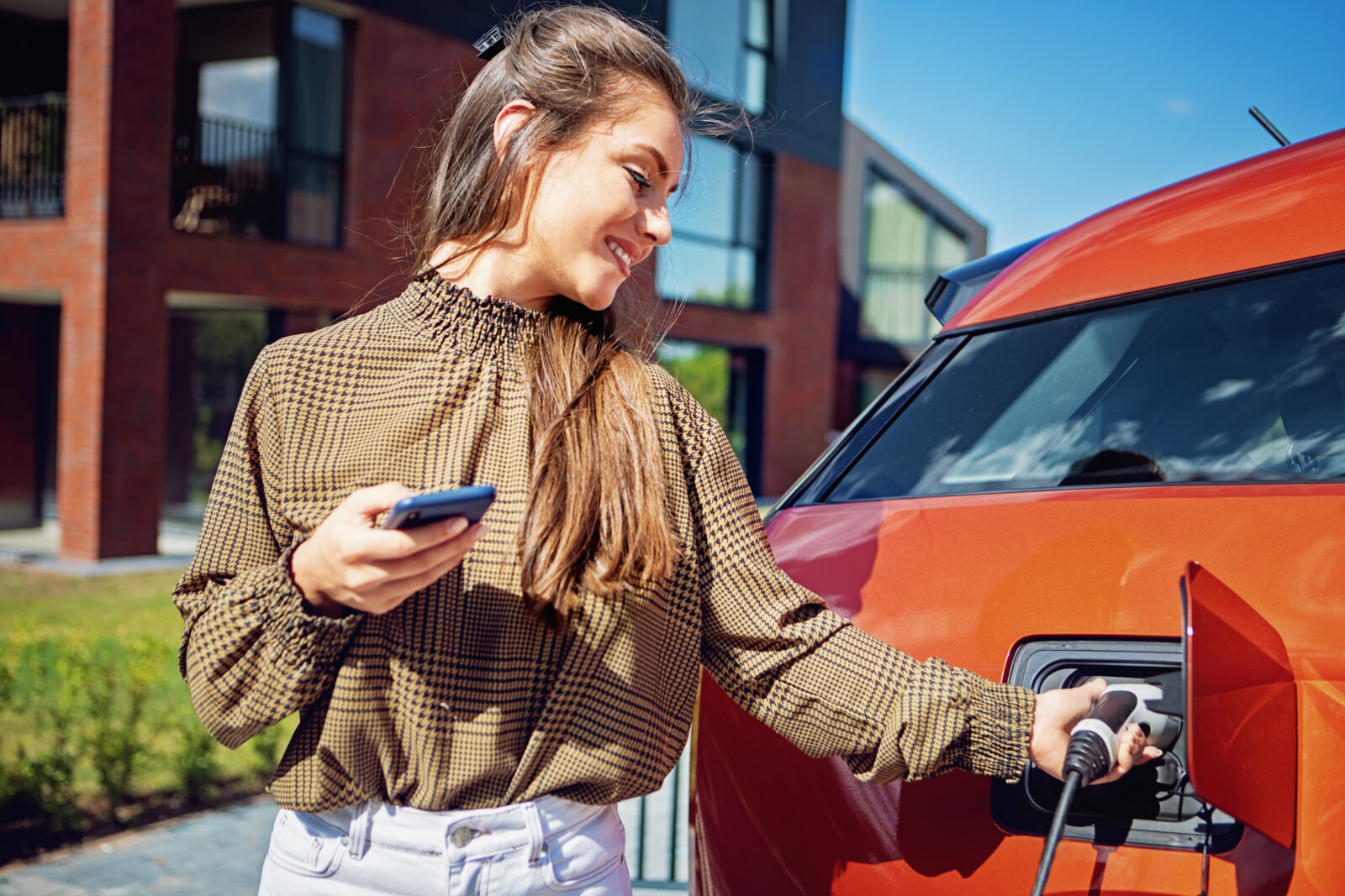 Vrouw laadt elektrische auto op bij moderne woning met laadpaal op de oprit