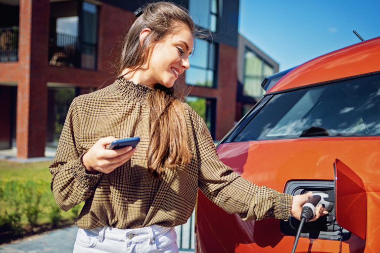 Vrouw laadt elektrische auto op bij moderne woning met laadpaal op de oprit