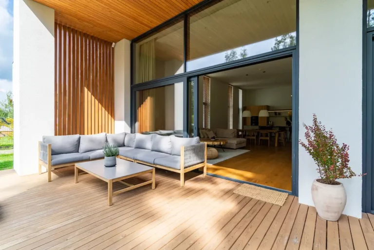 Houten vlonderterras met loungeset en moderne woning met grote schuifpui