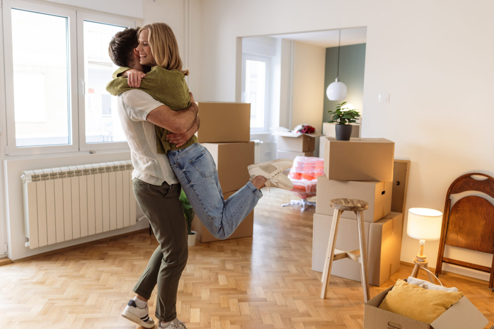 Stel dat een stel elkaar omhelst in hun nieuwe woning tussen verhuisdozen na de sleuteloverdracht.