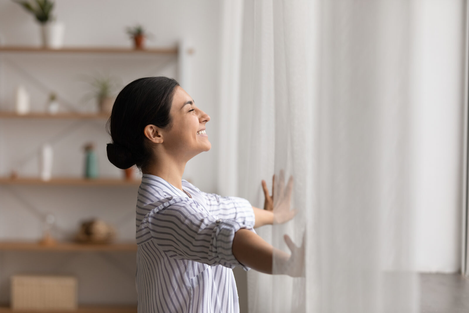 Vrouw opent lichte gordijnen in moderne woonkamer met daglicht