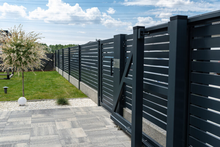 Moderne zwarte lamellen schutting in een strakke achtertuin met terras en gazon