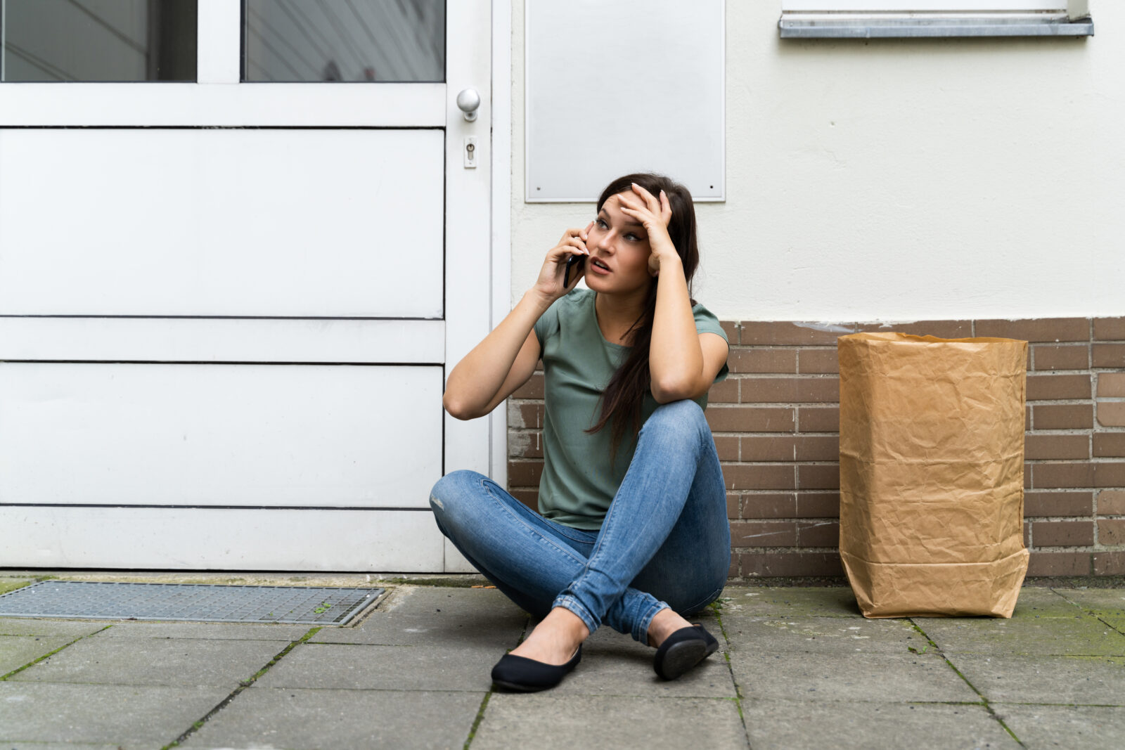 Buitengesloten vrouw zit voor haar woning terwijl ze belt om hulp