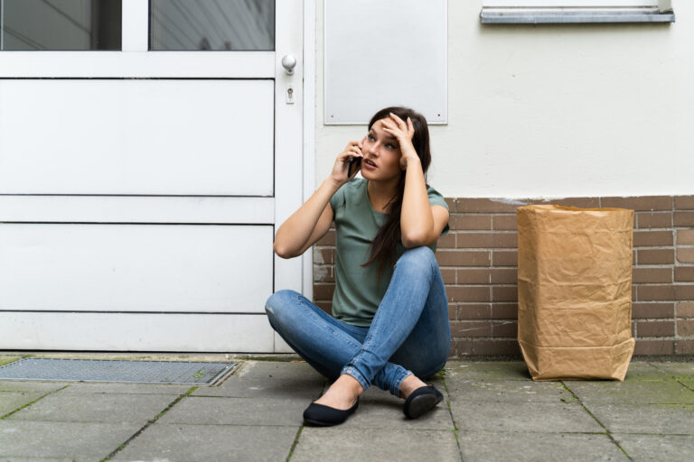 Buitengesloten vrouw zit voor haar woning terwijl ze belt om hulp