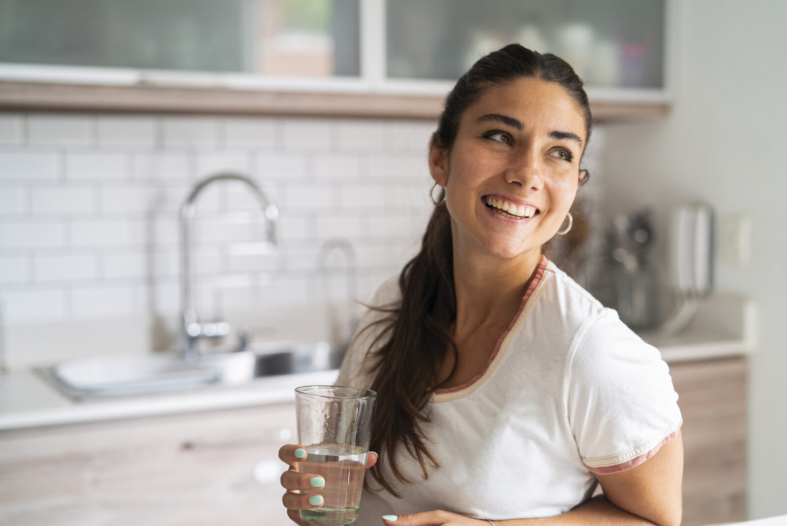Vrouw met glas kraanwater in moderne keuken als voorbeeld van waterkwaliteit in huis