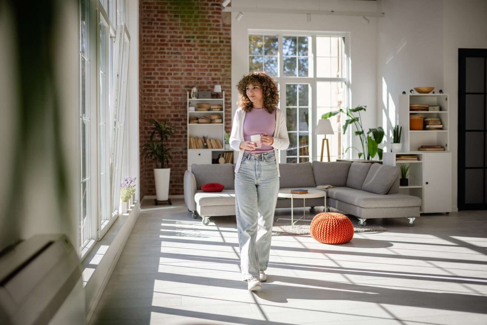 Vrouw loopt door een lichte woonkamer tijdens de voorjaarsschoonmaak met zonlicht dat naar binnen valt