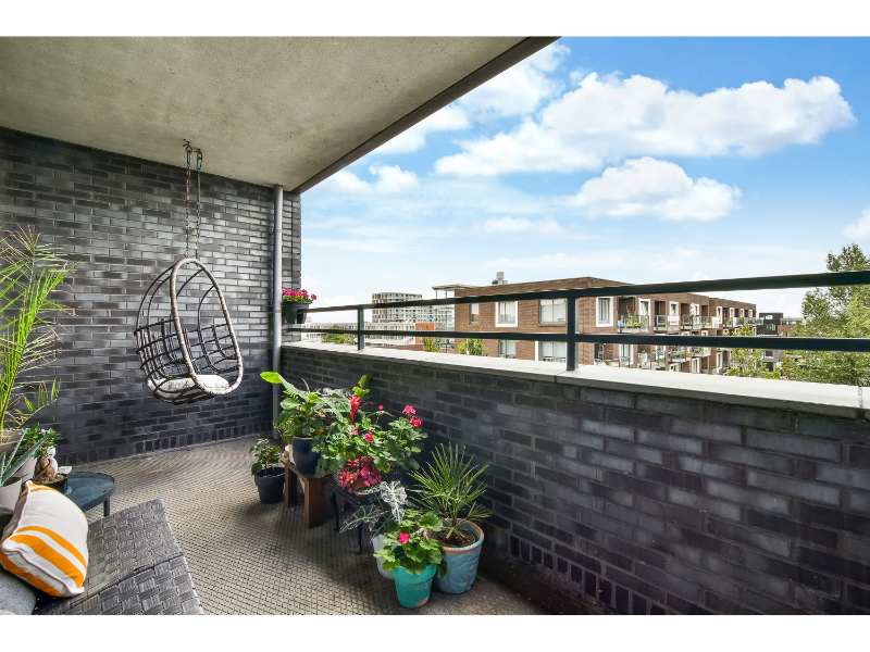 Balkon met hangstoel, planten en bakstenen muur, ingericht als comfortabele zitplek