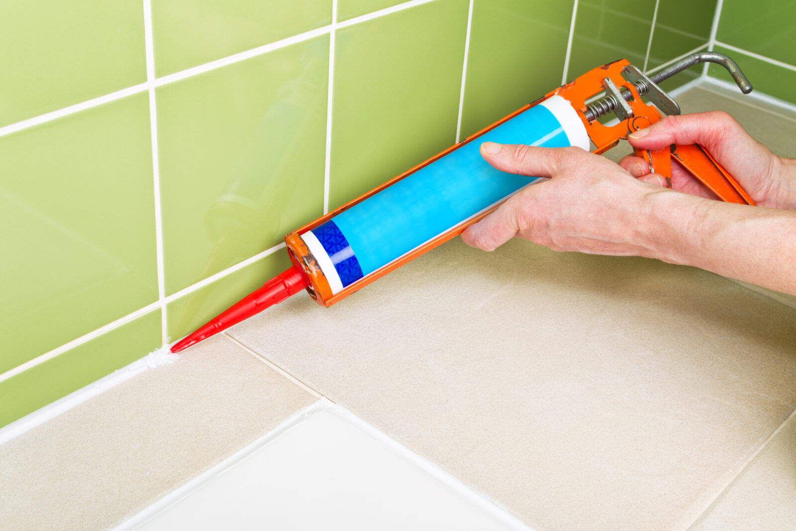 Iemand brengt kit aan langs tegels in een badkamer
