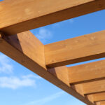 Houten balken van een overkapping in de tuin met blauwe lucht op de achtergrond