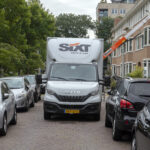 Verhuiswagen in een smalle woonstraat met geparkeerde auto’s