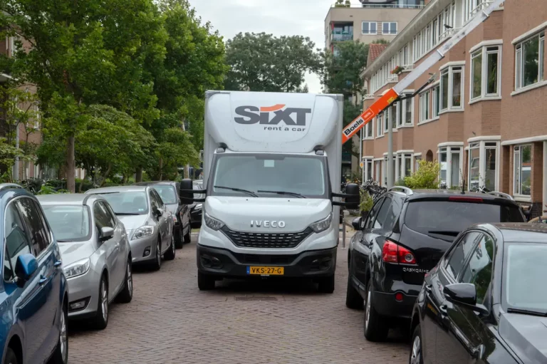 Verhuiswagen in een smalle woonstraat met geparkeerde auto’s