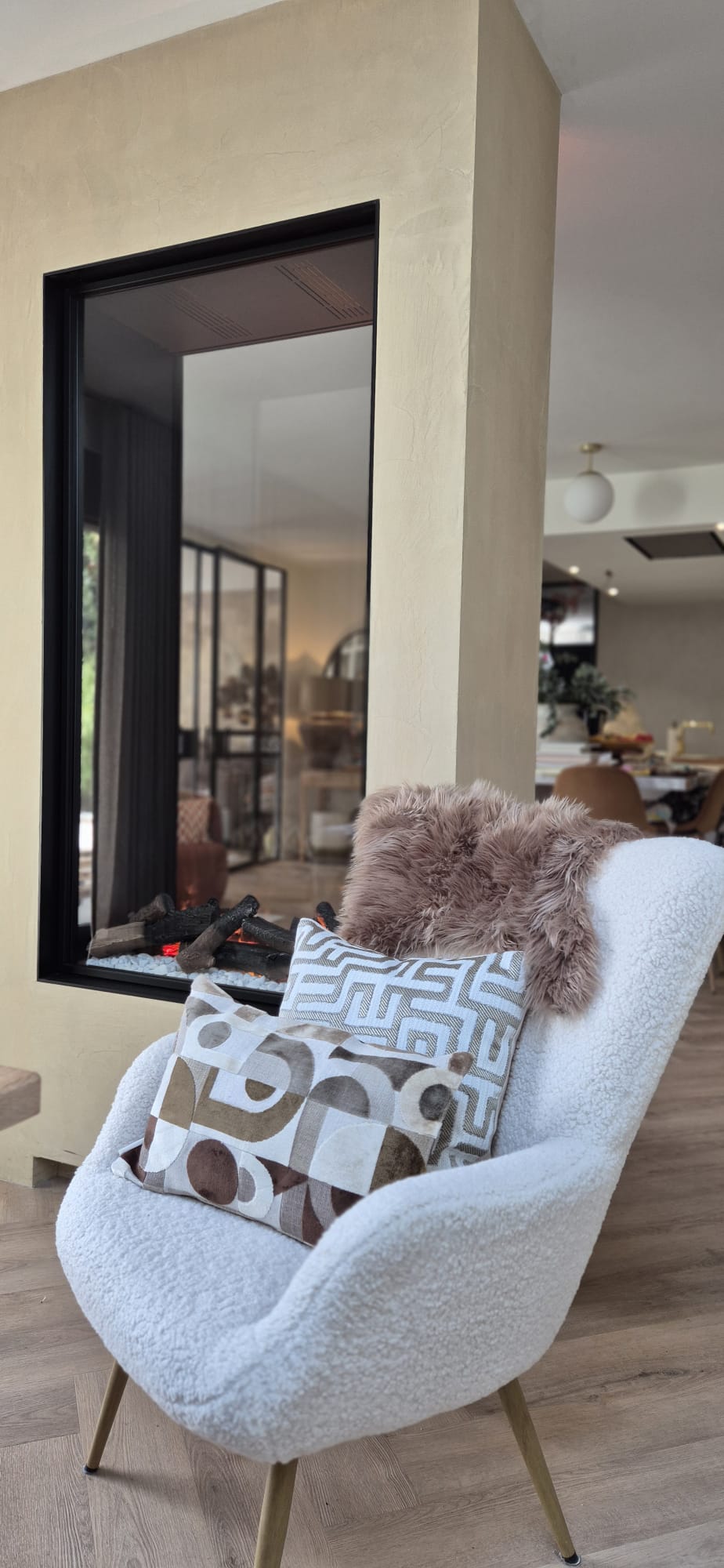 Witte fauteuil met sierkussens en plaid bij een moderne haard