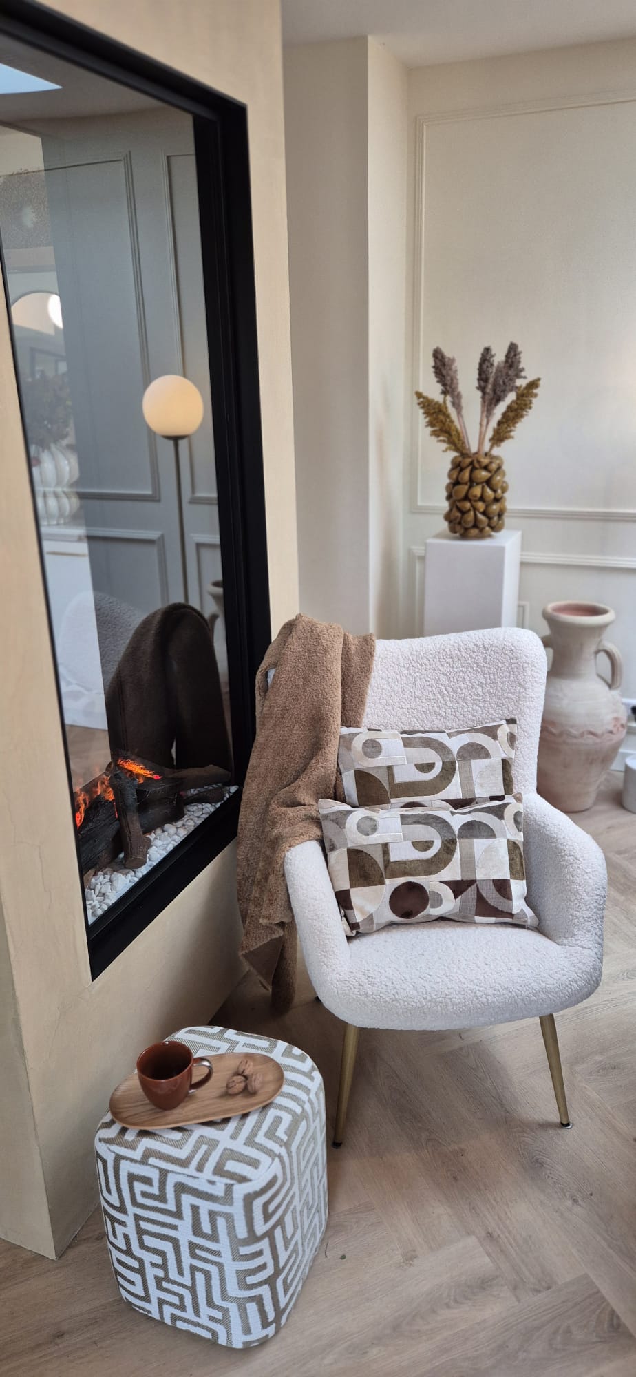 Witte fauteuil met sierkussens, plaid en poef bij de haard