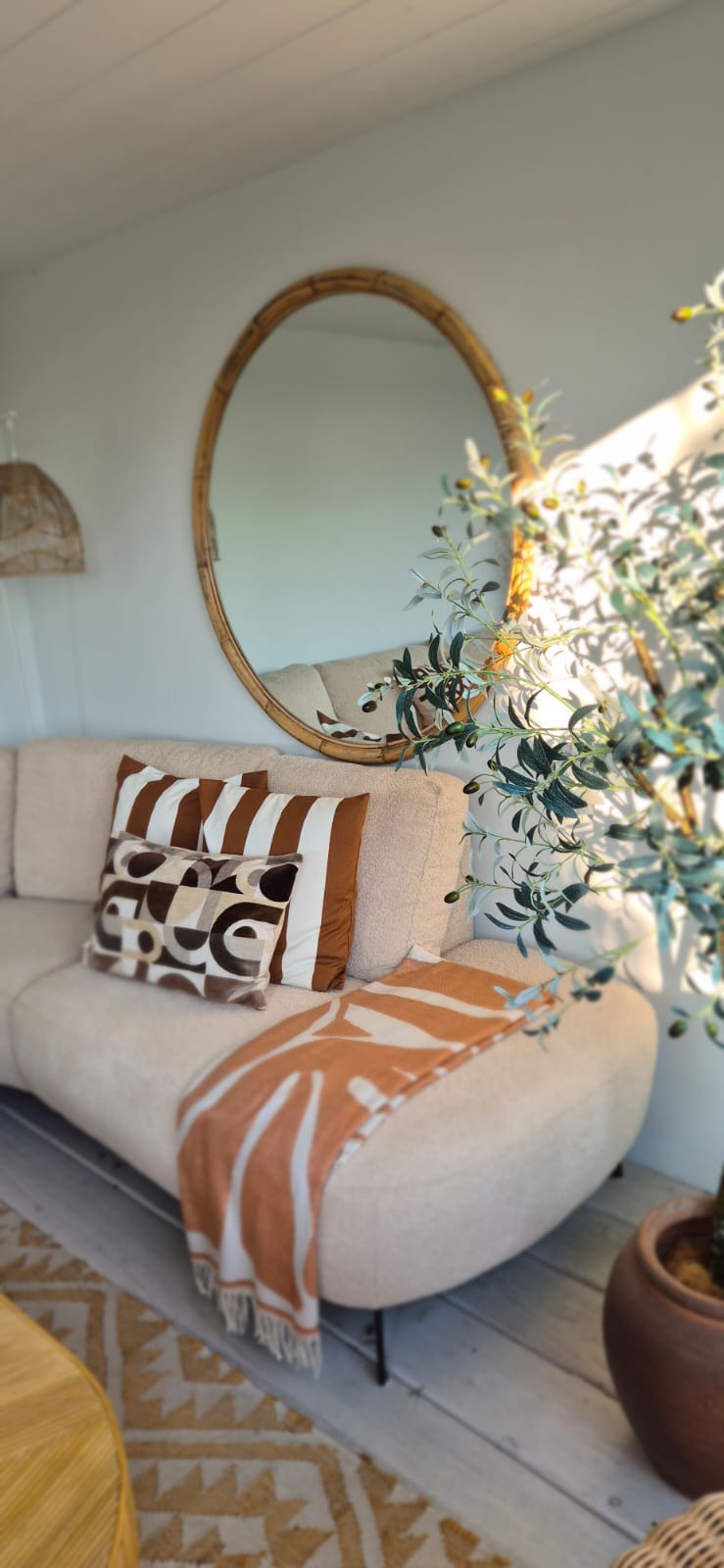 Lichte bank met sierkussens, plaid en ronde spiegel in een warm interieur