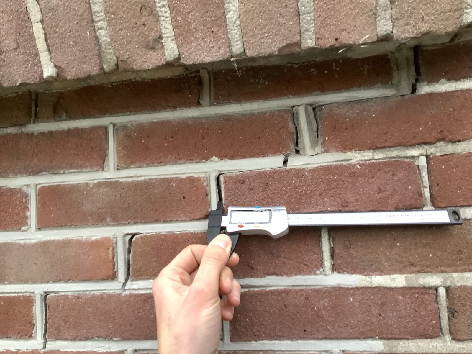 Scheur in metselwerk wordt gemeten tijdens een bouwkundige keuring