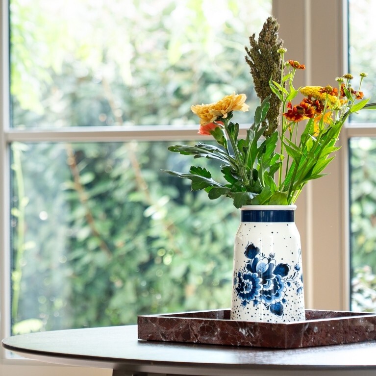 Delfts blauwe vaas met bloemen op tafel bij raam