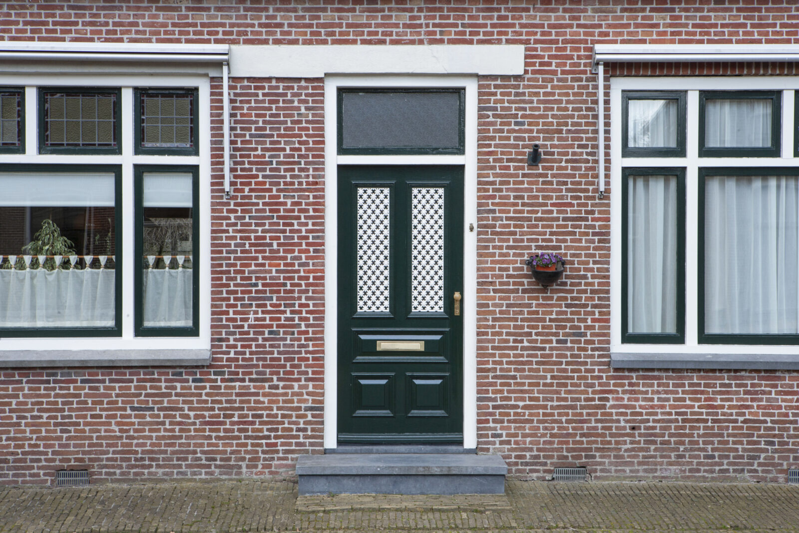 Groene voordeur met buitendeurbeslag bij een opgeknapte woning