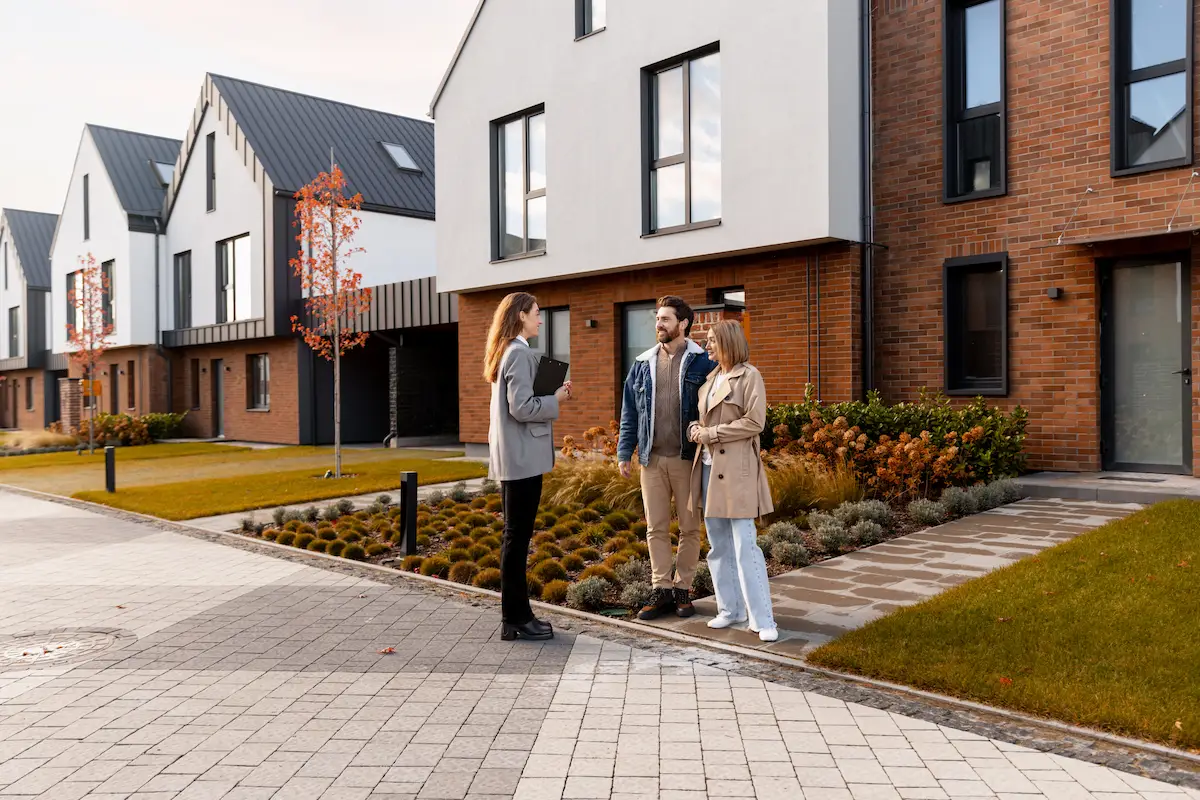 Makelaar en kopers staan voor een woning tijdens de sleuteloverdracht