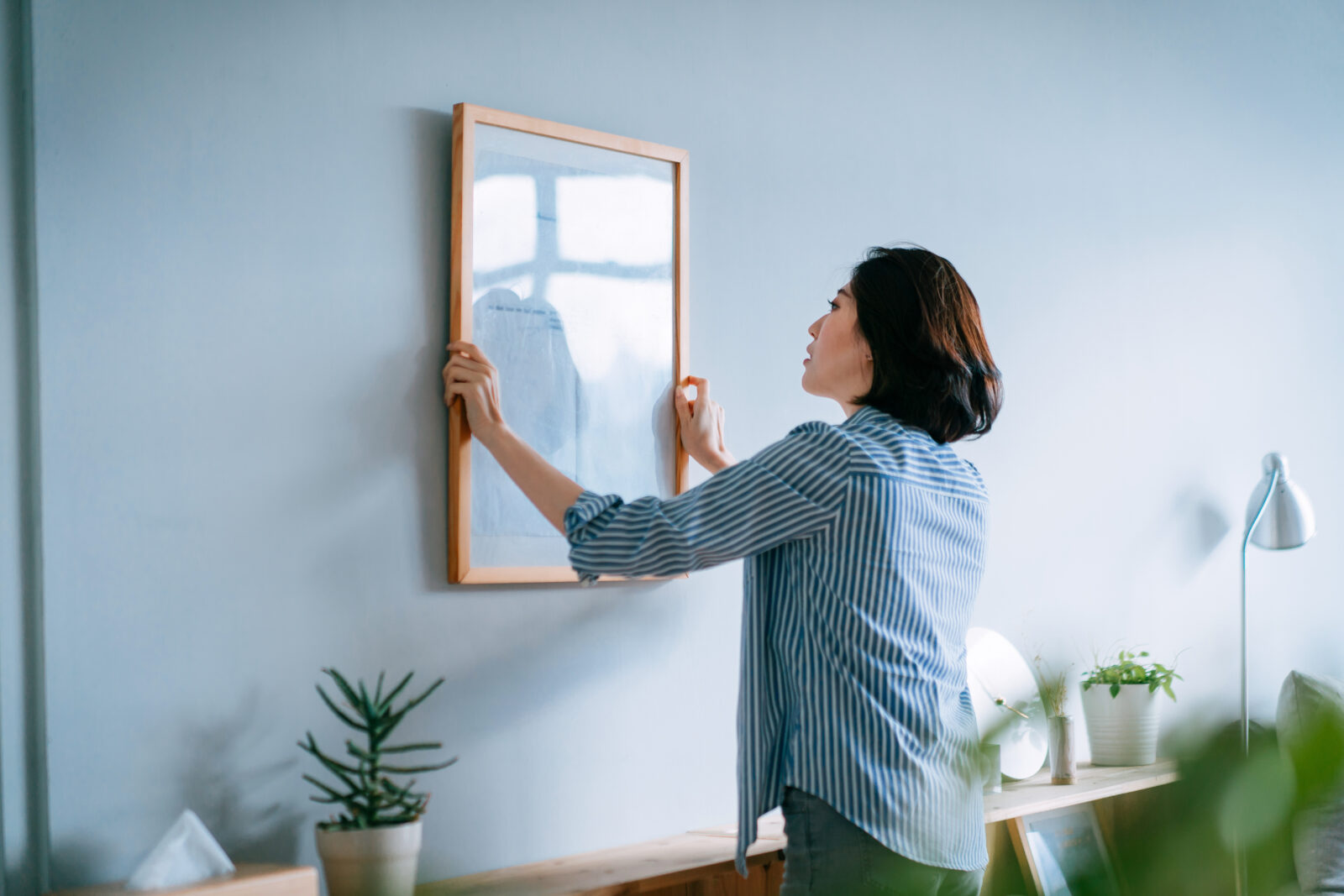 Vrouw hangt een schilderijlijst op aan een blauwe muur in een rustig interieur