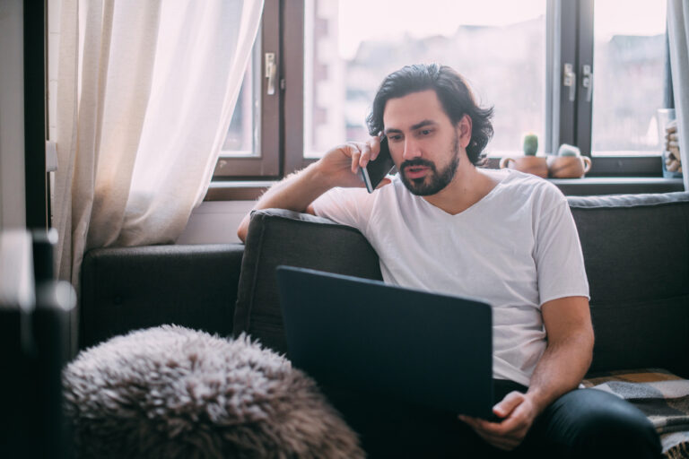 Zelfstandige voert thuis een zakelijk telefoongesprek met laptop op schoot